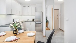 Una cocina moderna con armarios blancos, un refrigerador de acero inoxidable y un comedor con una mesa de madera dispuesta para dos.
