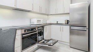 Una cocina moderna con armarios blancos, horno empotrado, microondas y refrigerador de acero inoxidable.