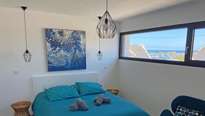 Une chambre avec un grand lit, une vue sur la mer et un fauteuil moderne.