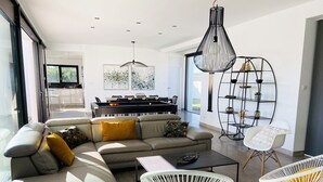 Un salon moderne avec un canapé d’angle, une table basse et deux chaises en fil de métal blanc.