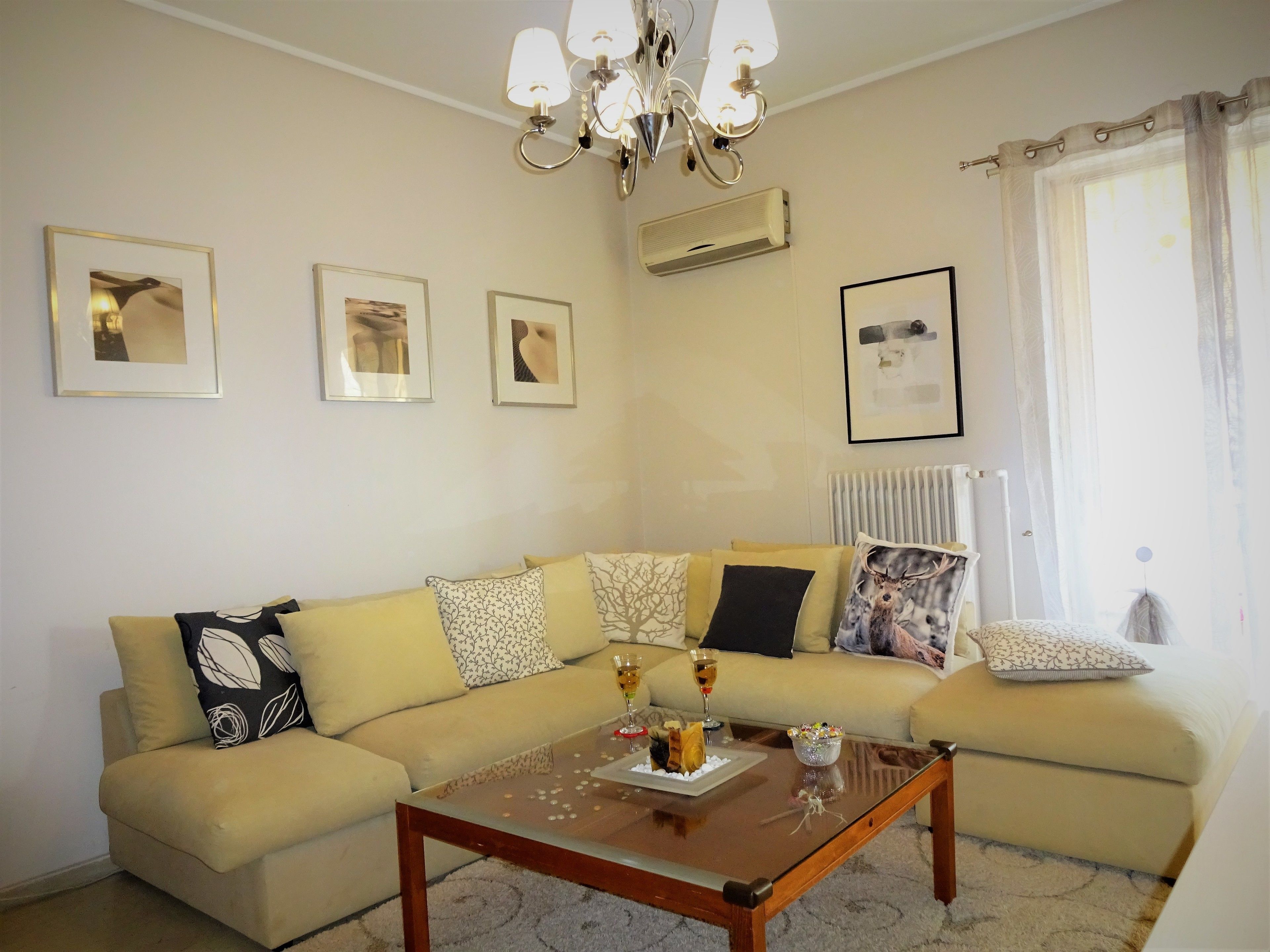 A living room with a beige sofa, a glass coffee table, and framed pictures on the wall.