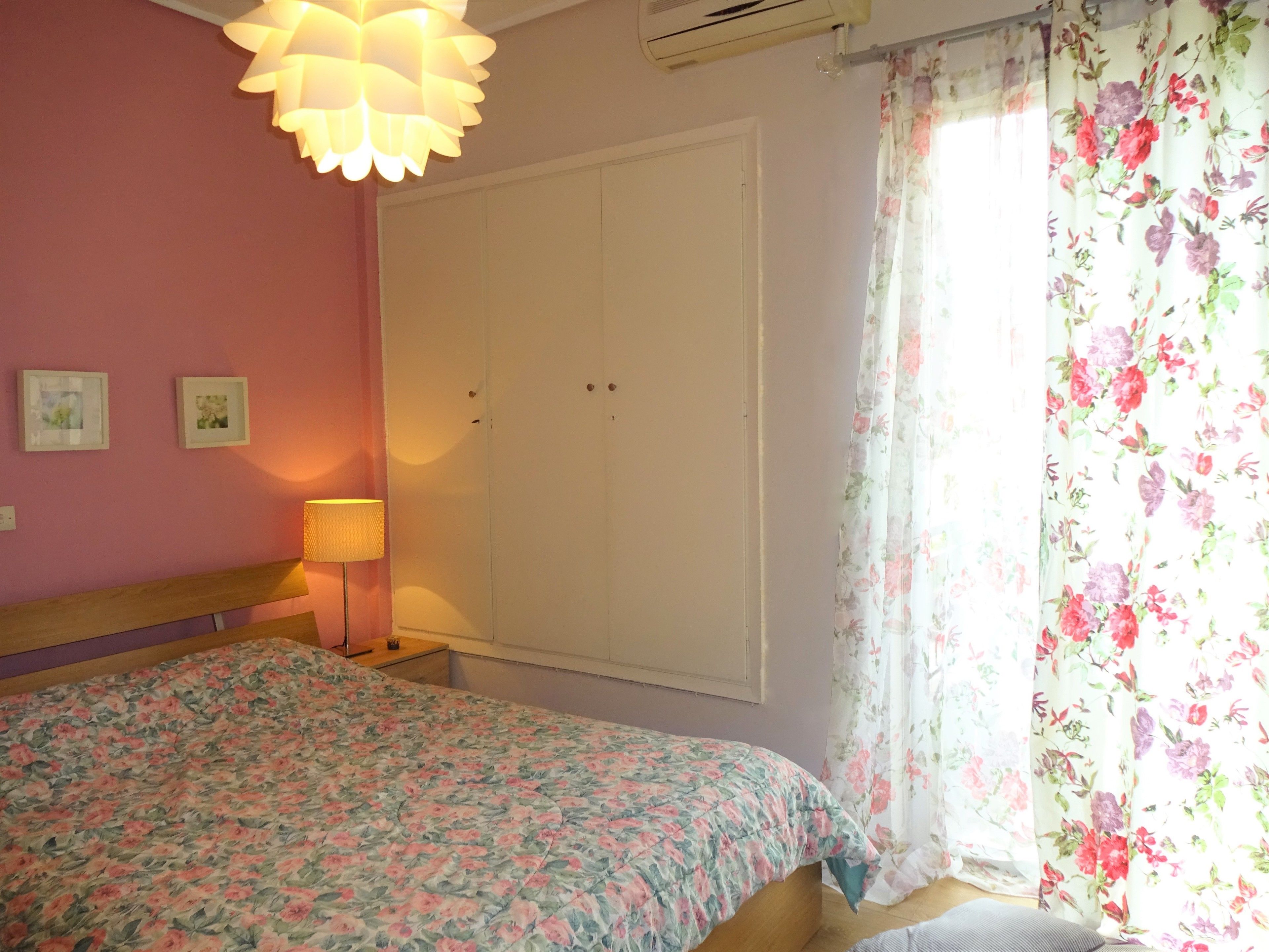 Un dormitorio con cama, armario, lámpara y ventana con cortinas estampadas.