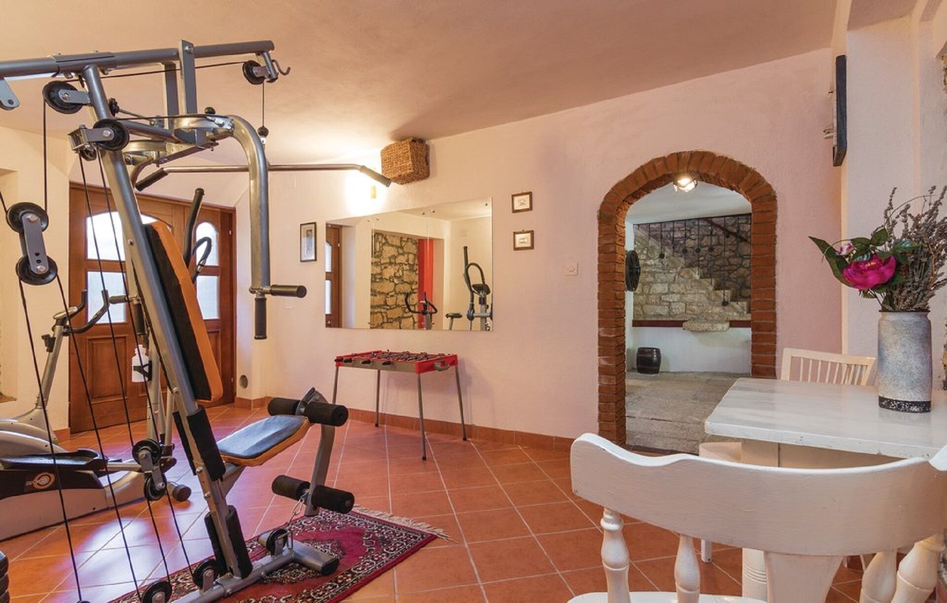 Une salle de sport à domicile équipée de matériel d’exercice, une table à manger avec des chaises et une vue sur un escalier en pierre.