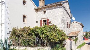 Ein traditionelles Steinhaus mit weißer Fassade und roten Fensterläden, umgeben von üppiger Vegetation und einer Steinmauer.