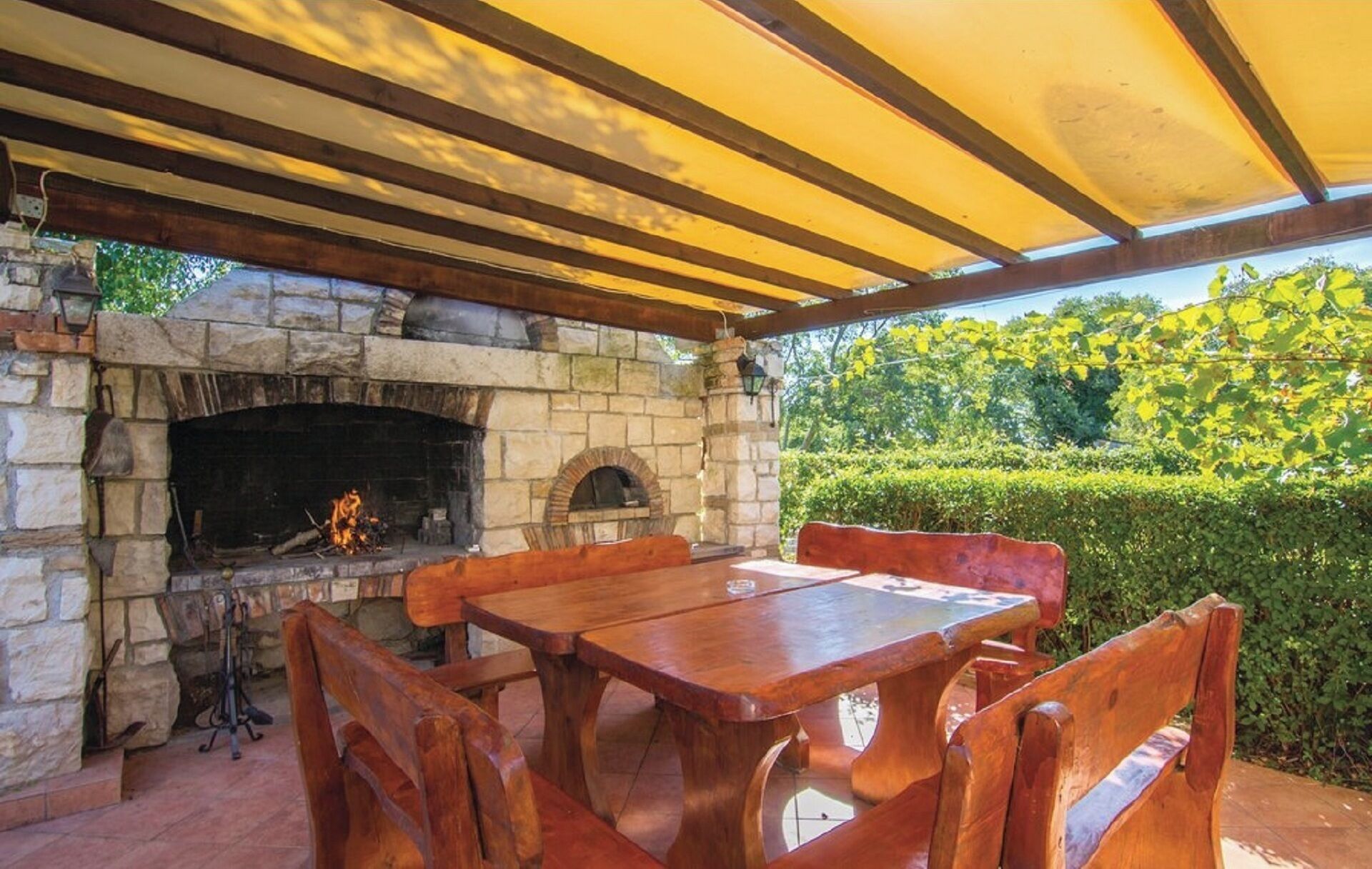 An outdoor stone fireplace with a table and chairs under a wooden pergola.