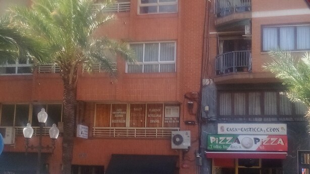 Un immeuble à plusieurs étages doté de balcons, d’un palmier et d’un espace extérieur aménagé pour s’asseoir.