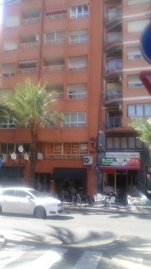 A multi-story building with balconies, a palm tree, and outdoor seating.