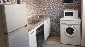 Une cuisine compacte équipée d’un réfrigérateur, d’une cuisinière, d’un évier, d’un four à micro-ondes et d’un lave-linge.