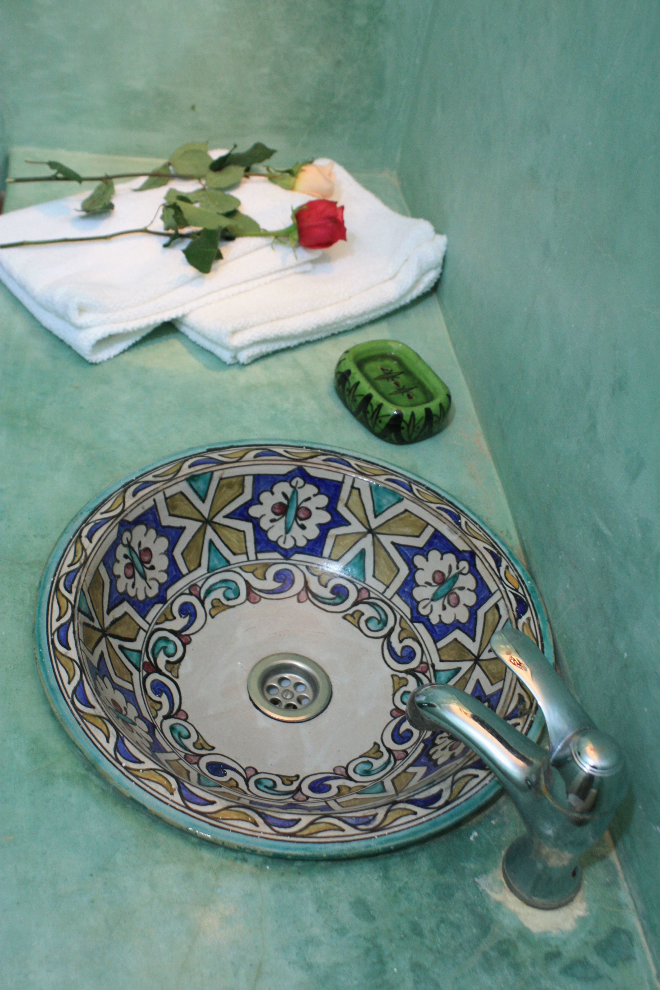 Un lavabo de salle de bain avec un récipient décoratif en faïence, un robinet et une rose posée sur une serviette.