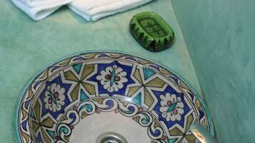 Un lavabo de salle de bain avec un récipient décoratif en faïence, un robinet et une rose posée sur une serviette.
