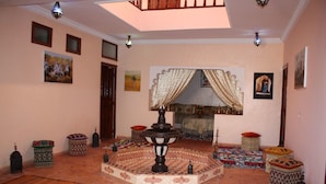 A room with a tiled floor, a central decorative fountain, patterned cushions, and wall-mounted artwork. - Auberge Benija (Anougal)