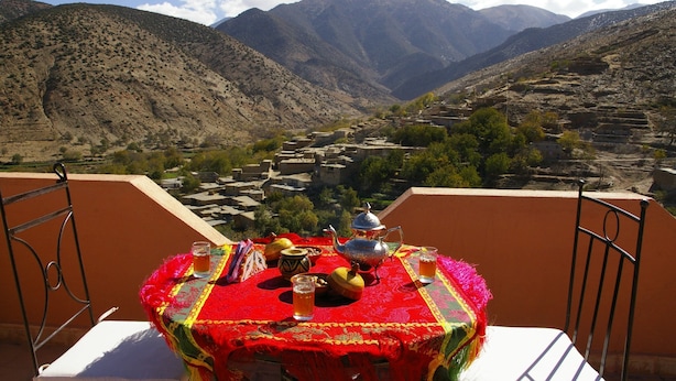 A table with a red tablecloth, a teapot, cups, and a view of a mountainous landscape. - Auberge Benija (Anougal)