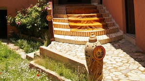 A building with a stone staircase leading to a balcony, surrounded by a garden with flowers and a decorative fire hydrant. - Auberge Benija (Anougal)