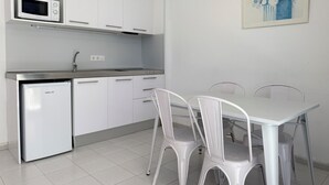 A compact kitchen with white cabinets, a microwave, a dishwasher, and a dining area with a white table and chairs. - Agi Rescator 220 Apartamento for rent in Roses Girona. (Rosas / Roses)