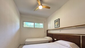 A bedroom with two beds, a ceiling fan, a window, and a framed picture on the wall. - Agi Rescator 220 Apartamento for rent in Roses Girona. (Rosas / Roses)