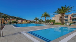 A swimming pool area with multiple pools, palm trees, and a building in the background. - Agi Rescator 220 Apartamento for rent in Roses Girona. (Rosas / Roses)