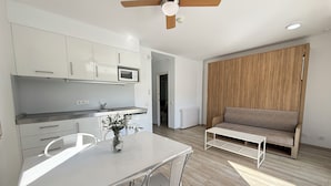 Een moderne keuken met witte kasten, een eettafel met stoelen, een plafondventilator en een wand van houtpanelen.
