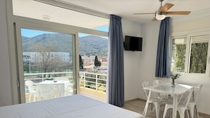 Hotelkamer met een bed, een televisie, een balkon met een tafel en stoelen, en uitzicht op de bergen.