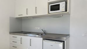 Een keuken met witte kastjes, een magnetron, een roestvrijstalen spoelbak en een koelkast.