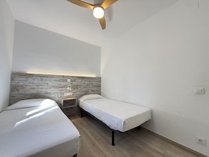 A small, modern room with two single beds, a wooden headboard, a ceiling fan, and a wall-mounted light fixture. - Agi Rescator 107 Apartamento for rent in Roses Girona. (Rosas / Roses)