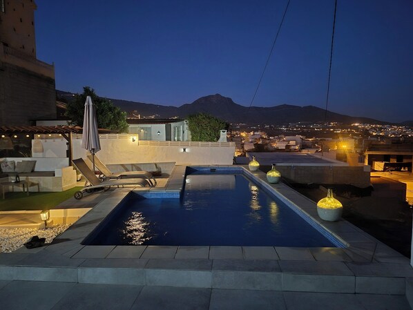 A rooftop pool with a view of a cityscape and mountains at dusk.