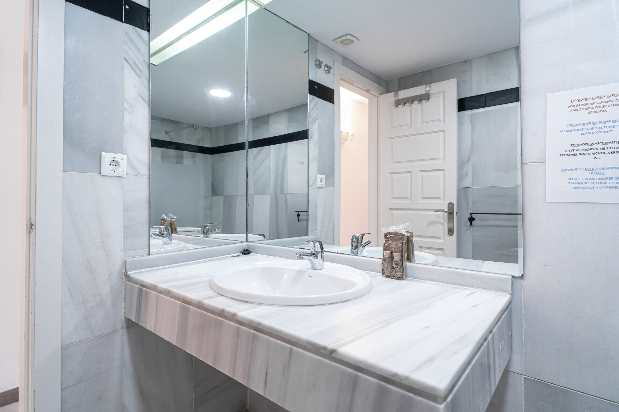 Une salle de bain moderne avec deux lavabos, un grand miroir et une porte blanche.