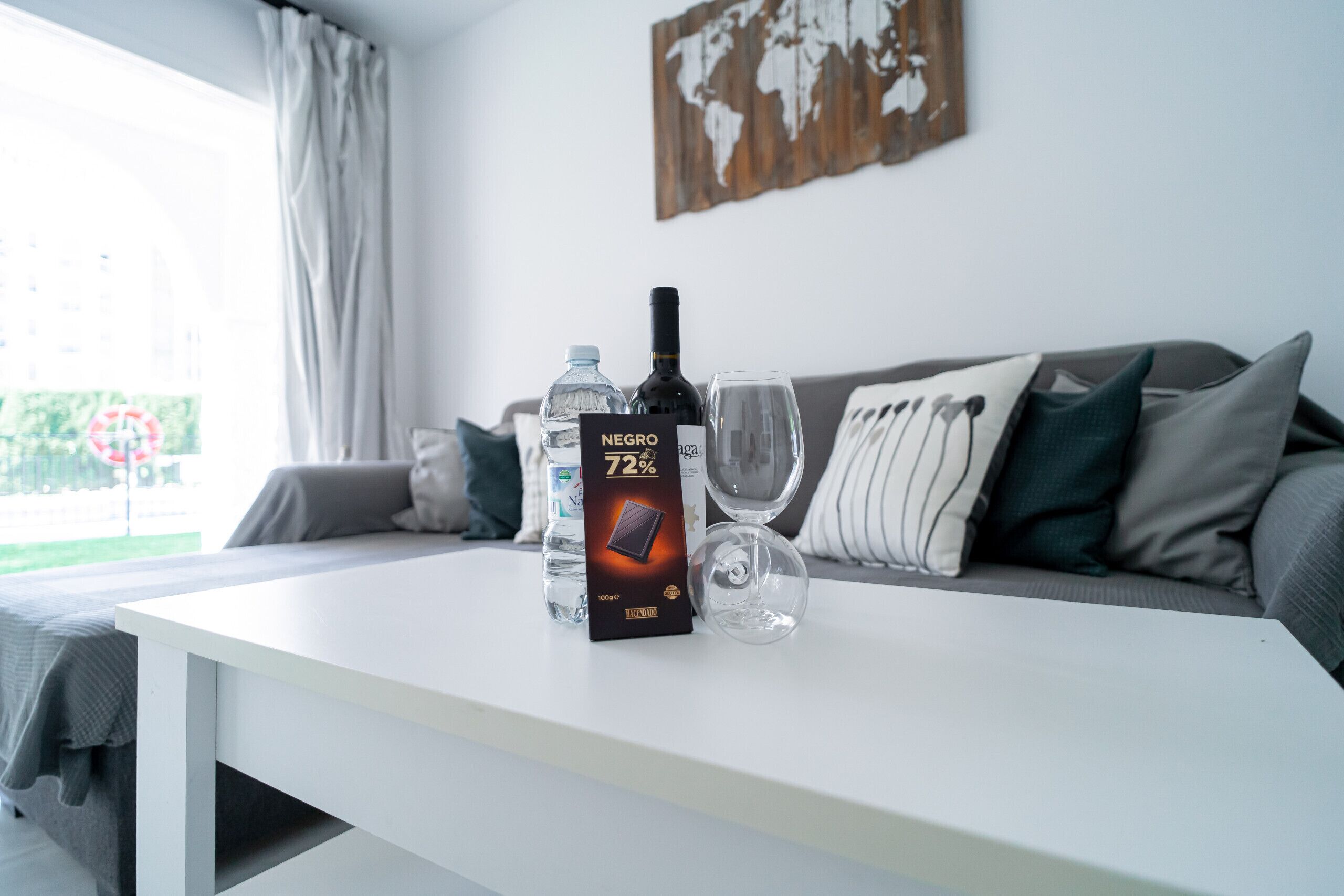 Een tafel met een doos chocolade, een fles wijn en twee glaasjes.