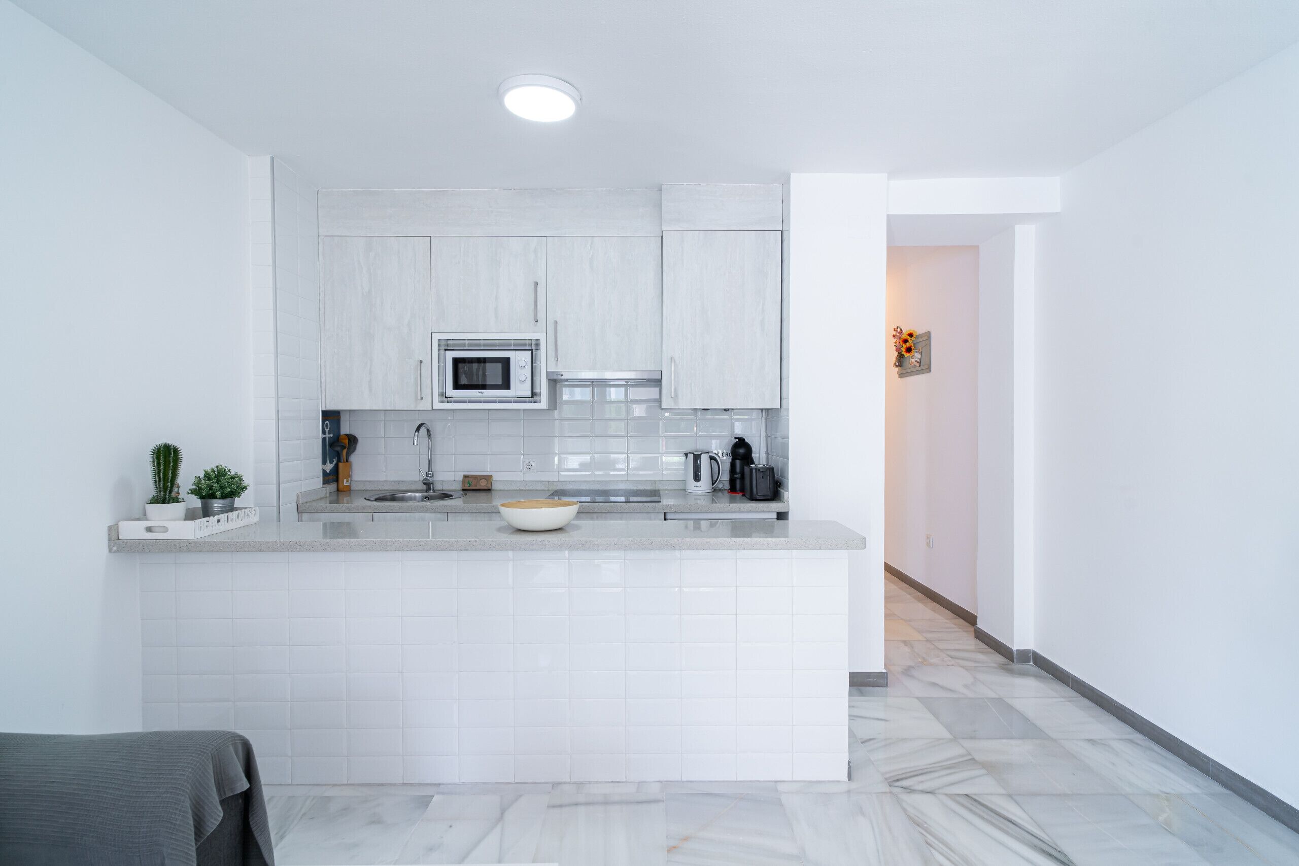 A modern kitchen with white cabinetry, a central island, a microwave, and a kettle.