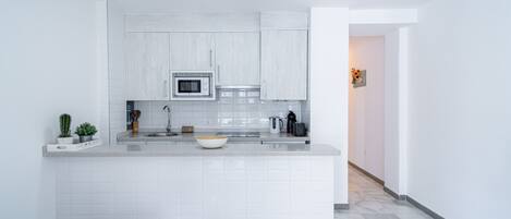 A modern kitchen with white cabinetry, a central island, a microwave, and a kettle.