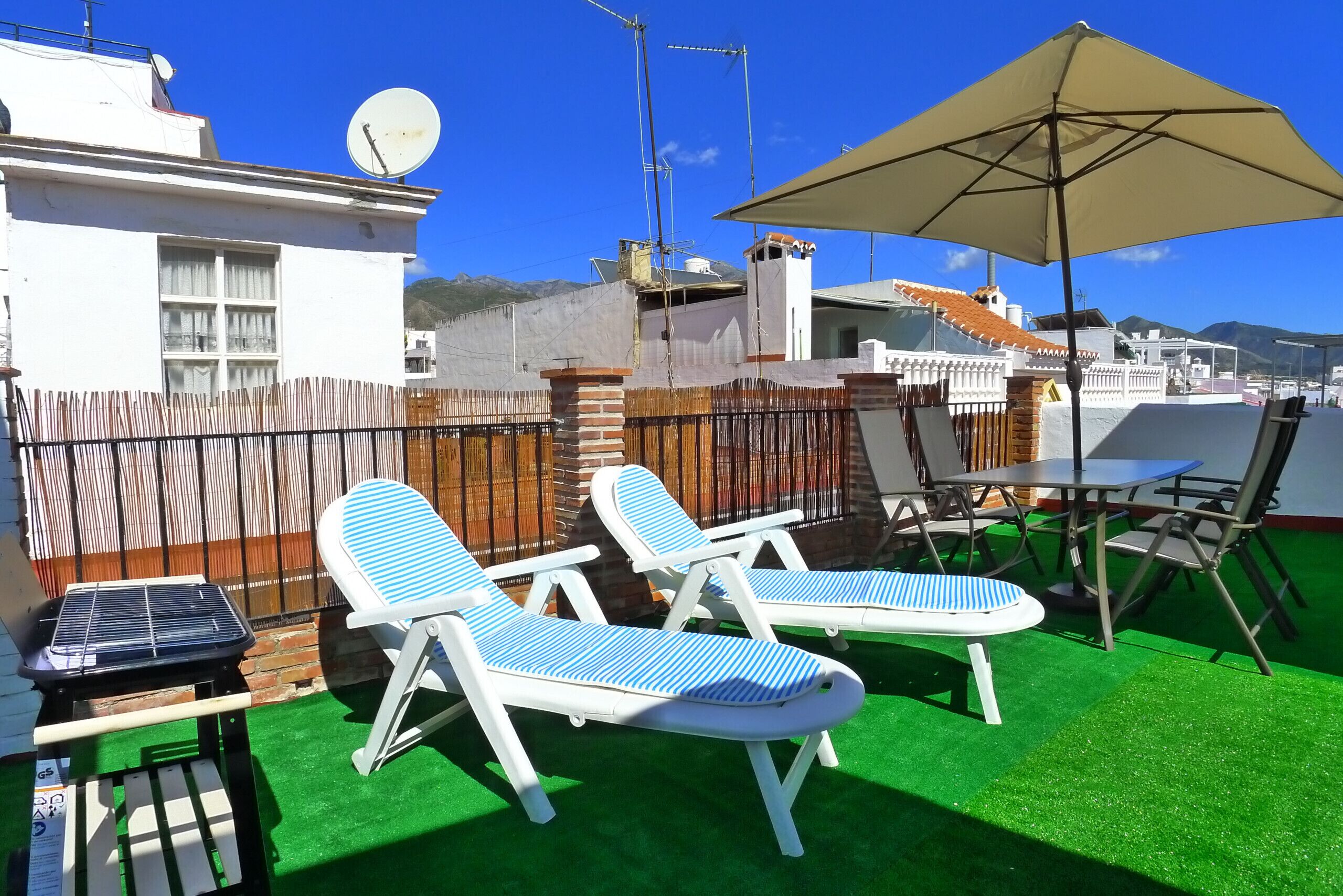 Eine Dachterrasse mit zwei Liegestühlen, einem Tisch und einem Sonnenschirm.