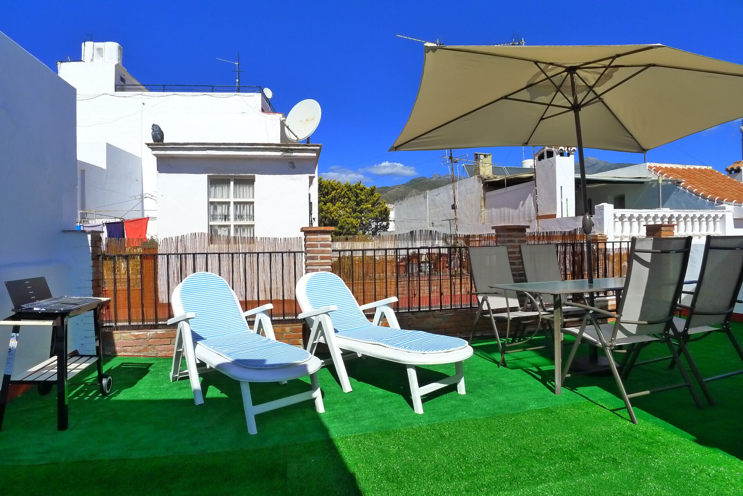 Une terrasse avec deux chaises longues, une table et un parasol.