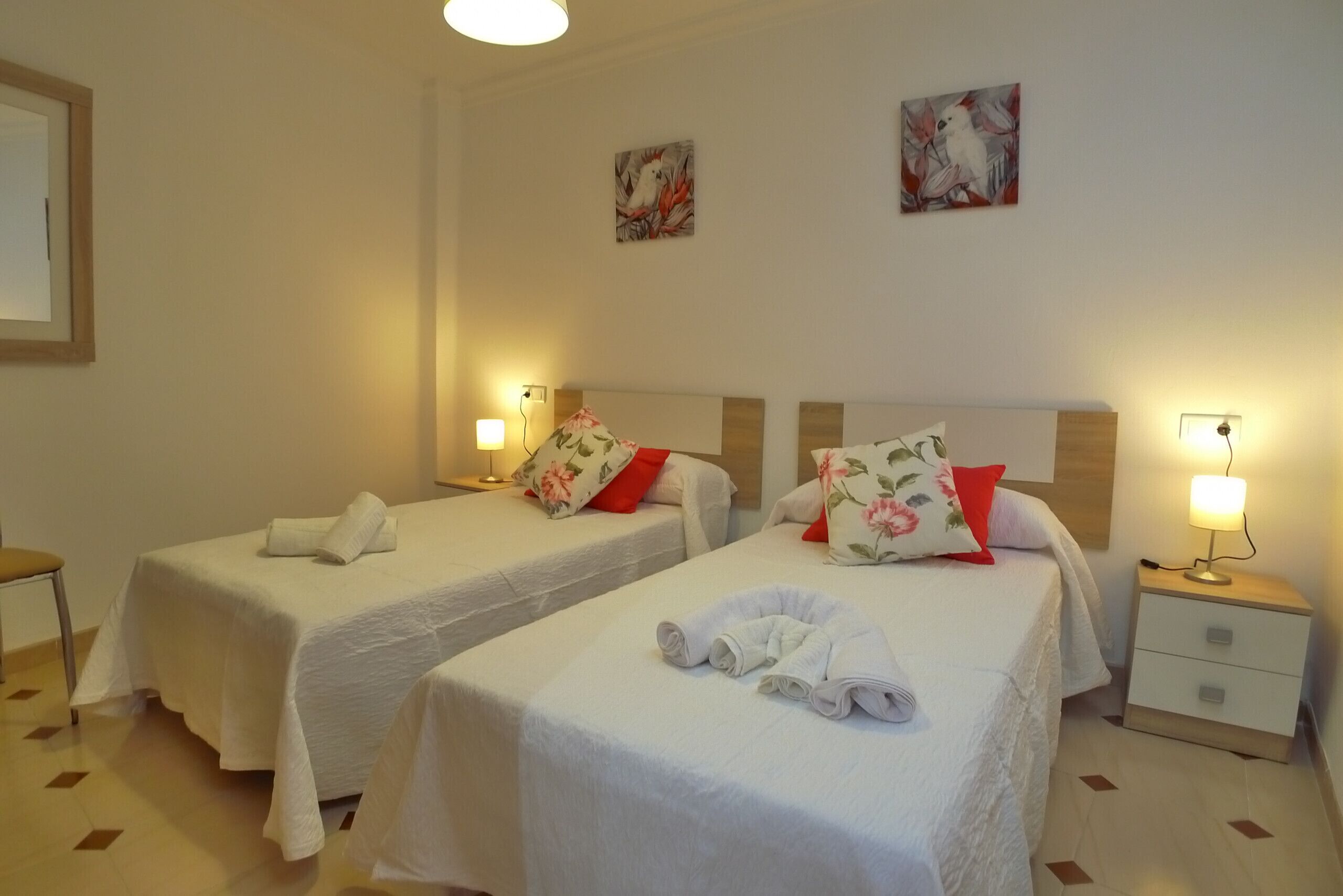 Ein Hotelzimmer mit zwei Einzelbetten, jeweils mit Kissen und einer Nachttischlampe.