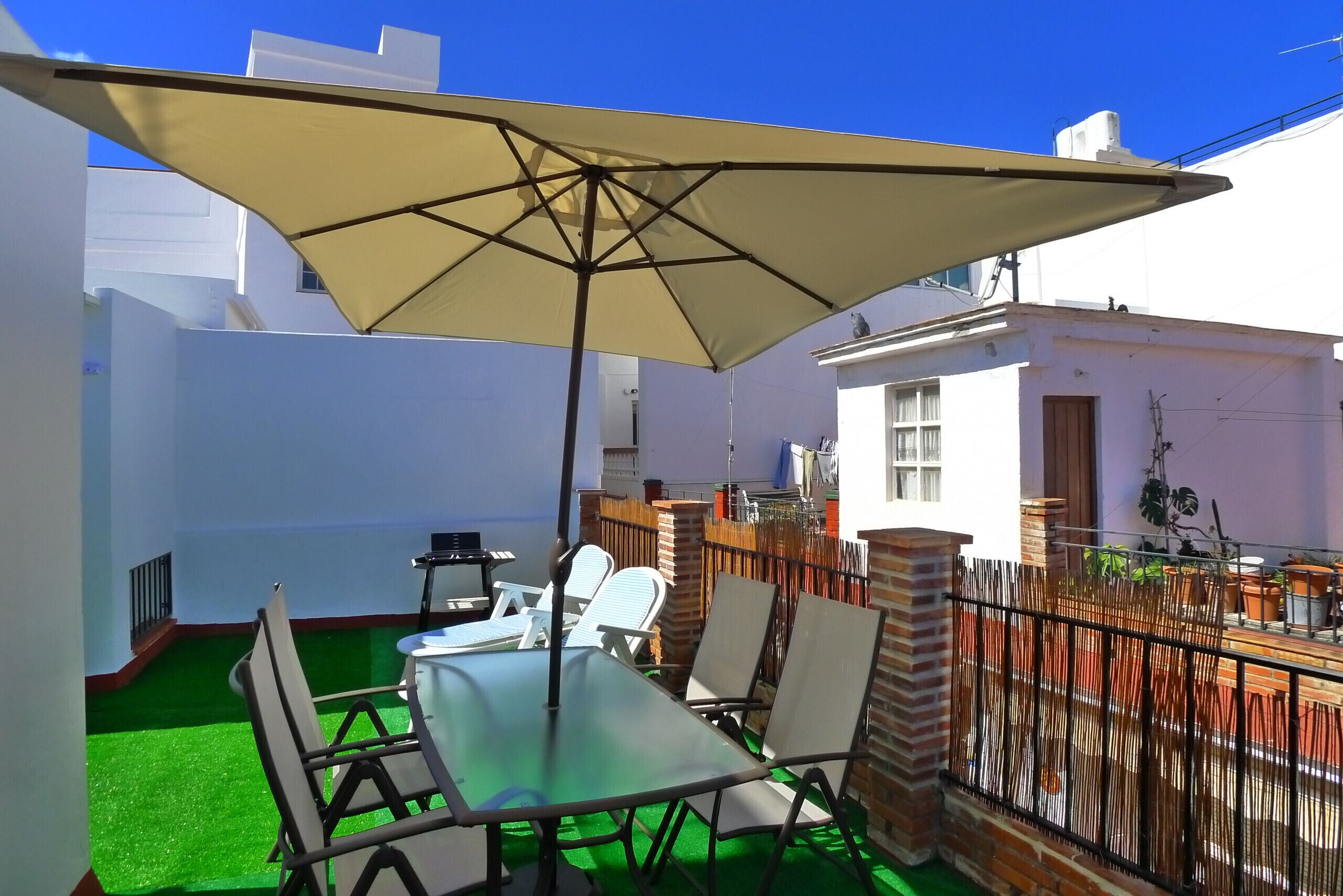A patio with a table and chairs, a large umbrella, and a green artificial turf.