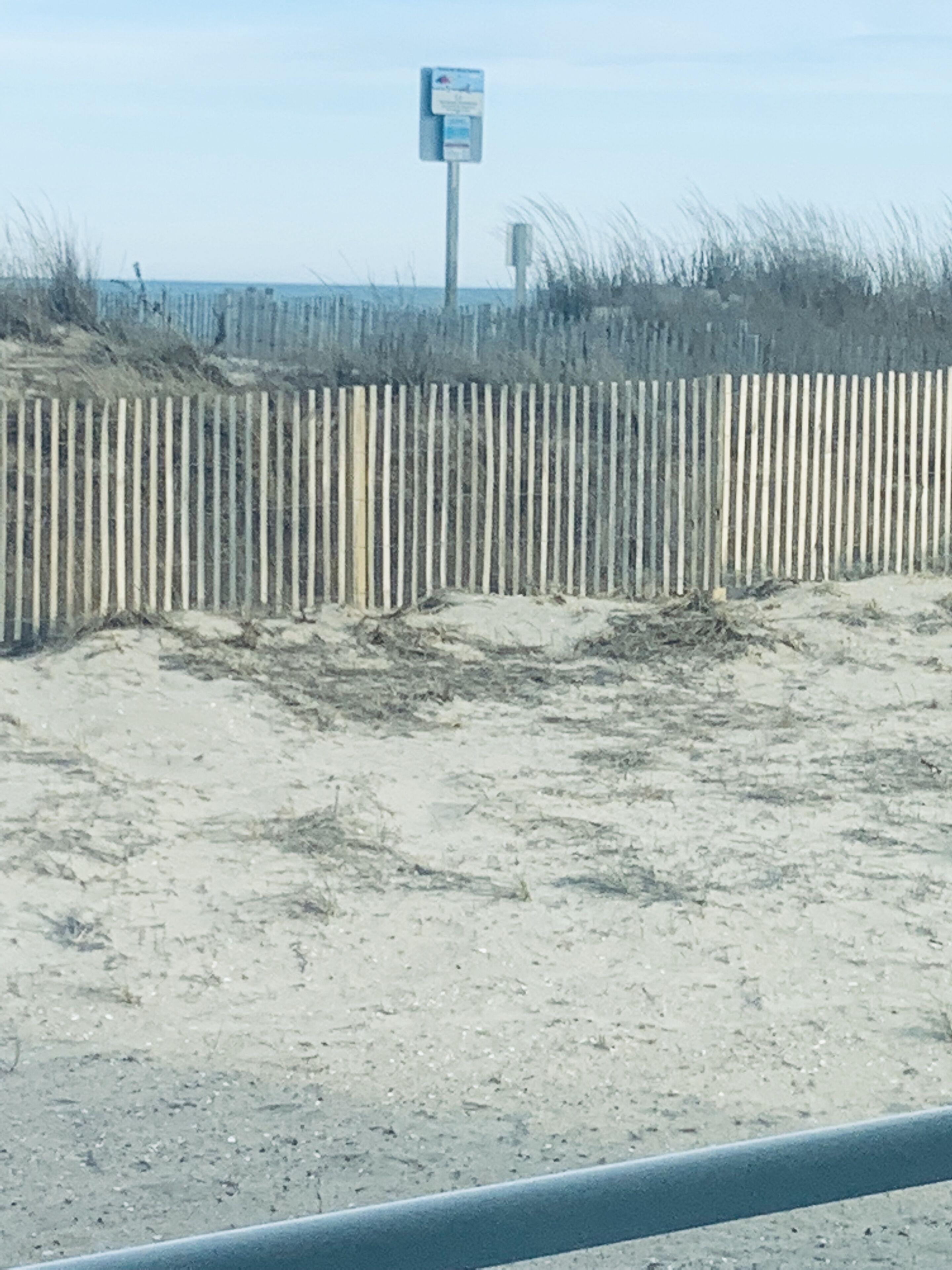 Una playa arenosa con una valla de madera y un letrero al fondo.