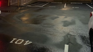 A multi-story parking garage with a wet surface, marked parking spaces, and a gated entrance.