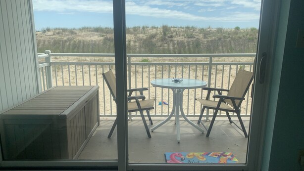 A balcony with a table and chairs, a wooden bench, and a view of the beach and dunes.