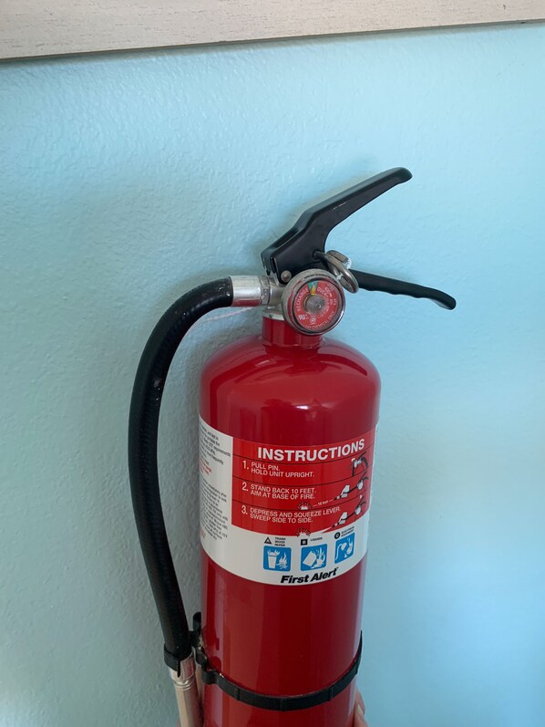 Estintore rosso montato su una parete con istruzioni e simboli di sicurezza.