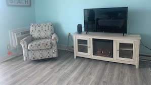 A living room with a patterned armchair, a flat-screen TV on a wooden cabinet, and a fireplace.