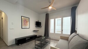 Een moderne woonkamer met een bank, een televisie, een plafondventilator en een balkon met gordijnen.