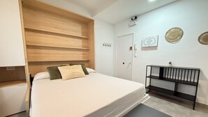 Een slaapkamer met een bed, een houten hoofdbord, een nachtkastje, een klein plankje en een deur.