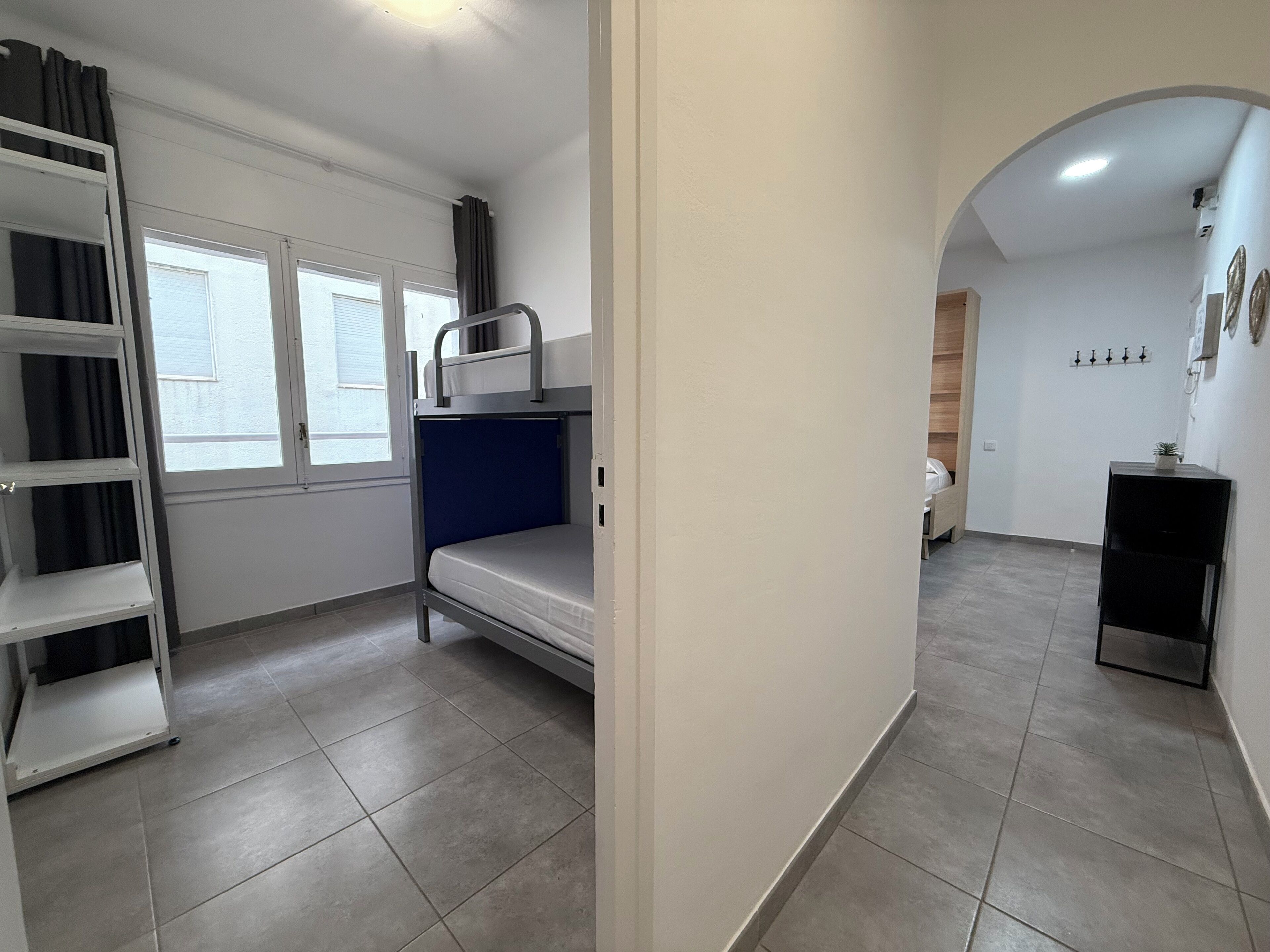 Una habitación pequeña con literas, ventana, kitchenette y puerta que da a otra habitación.