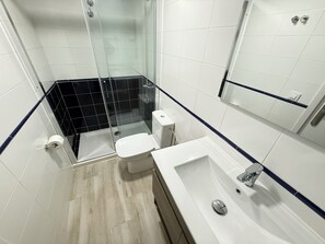 Un baño moderno con cabina de ducha de vidrio, inodoro blanco y lavamanos con espejo.
