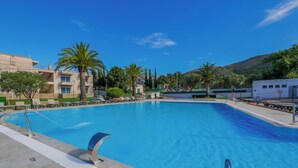 Une piscine à l’eau d’un bleu cristallin, entourée de palmiers et bordée d’un bâtiment doté de balcons.