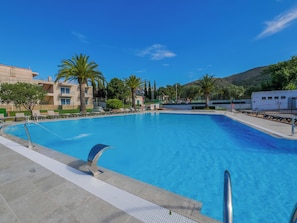 A swimming pool with clear blue water, surrounded by palm trees and a building with balconies. - Agi Rescator 215 Apartamento for rent in Roses Girona. (Rosas / Roses)
