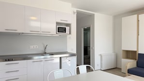 Une cuisine moderne avec des meubles blancs, un four à micro-ondes et un évier. On y trouve une table à manger avec des chaises, ainsi qu’un canapé bleu dans le salon attenant.