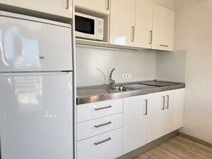 Eine Küche mit weißen Schränken, einer Edelstahl-Spüle, einer Mikrowelle und einem Kühlschrank.