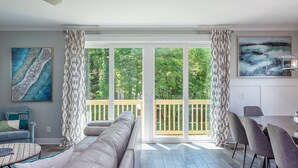 Een ruime woonkamer met een grote schuifpui naar een balkon, een bank, een eettafel met stoelen en kunstwerken aan de wanden.