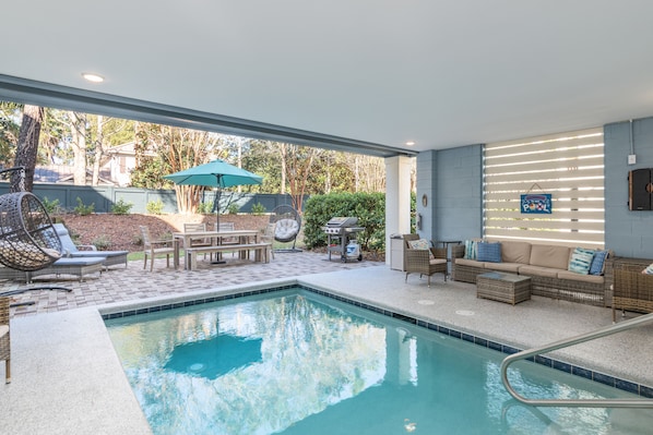 Un espace piscine comprenant des chaises longues, une table avec des chaises et un barbecue.