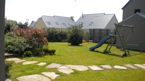 Een achtertuin met een pad van stenen, een glijbaan en een houten schommelset.