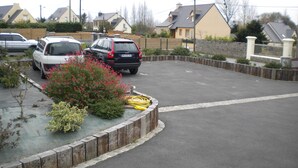 Een parkeerplaats met twee auto's, een bloembed en een tuinslang op de grond.